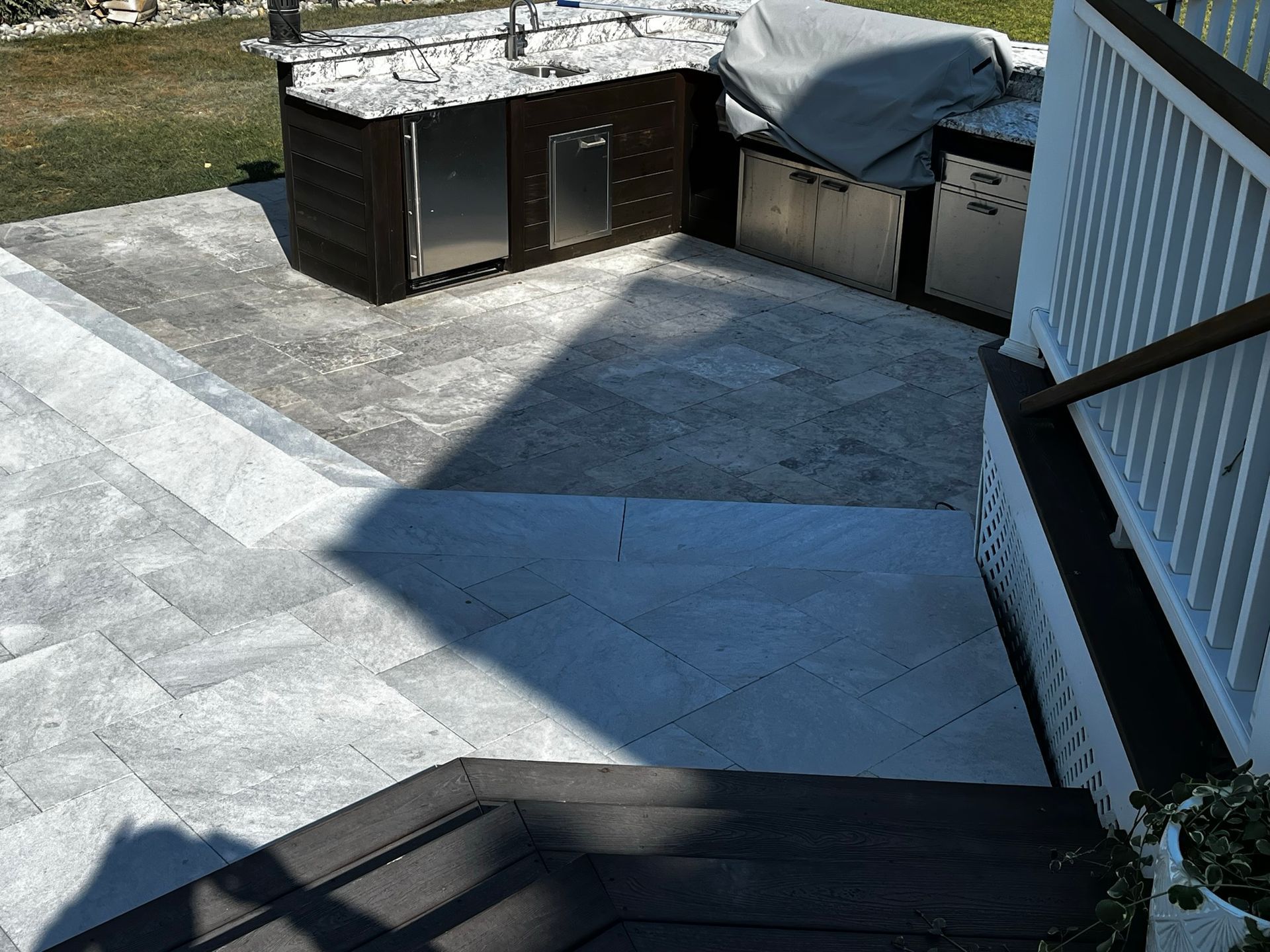 Patio with built-in outdoor kitchen. Gray pavers, wood steps, white railing, dark cabinets with stainless steel appliances.