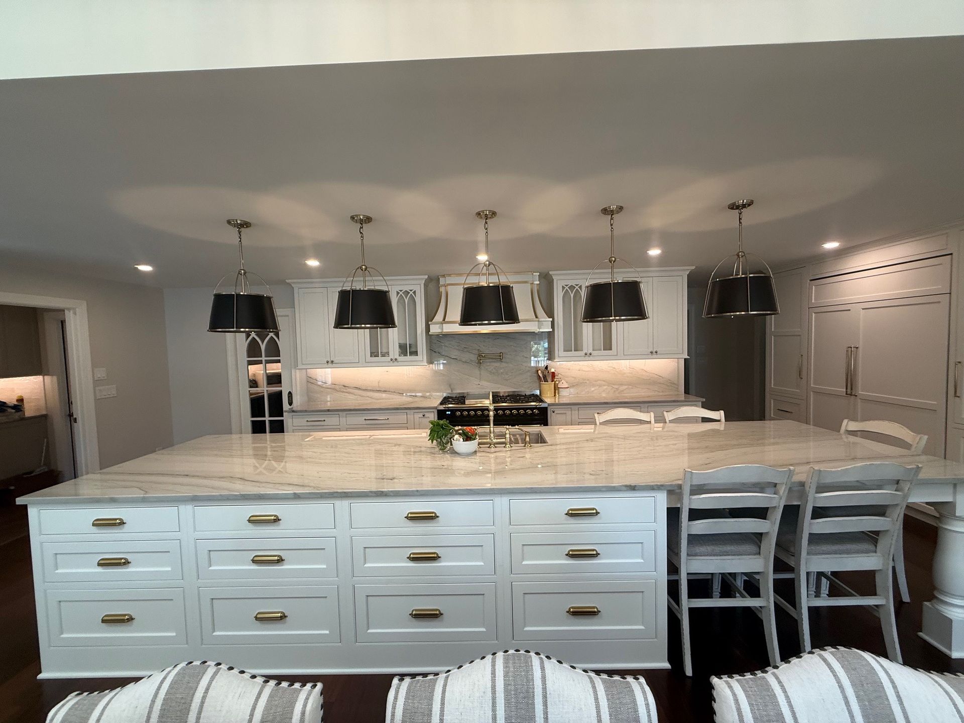 White kitchen with island, six black pendant lights, granite countertop, and white cabinets.