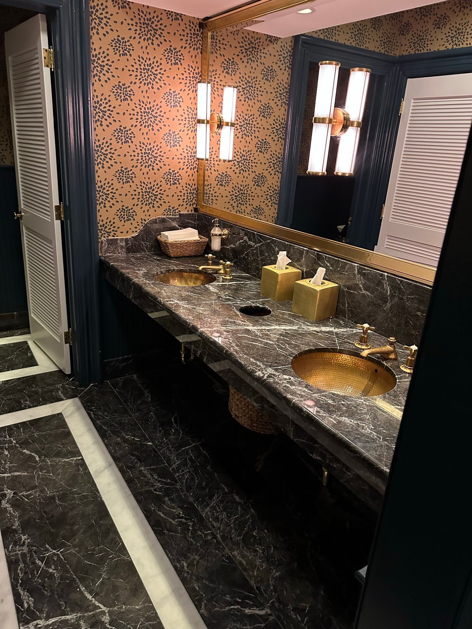 Bathroom with marble counter and gold fixtures, mosaic backsplash. Black and white patterned floor.
