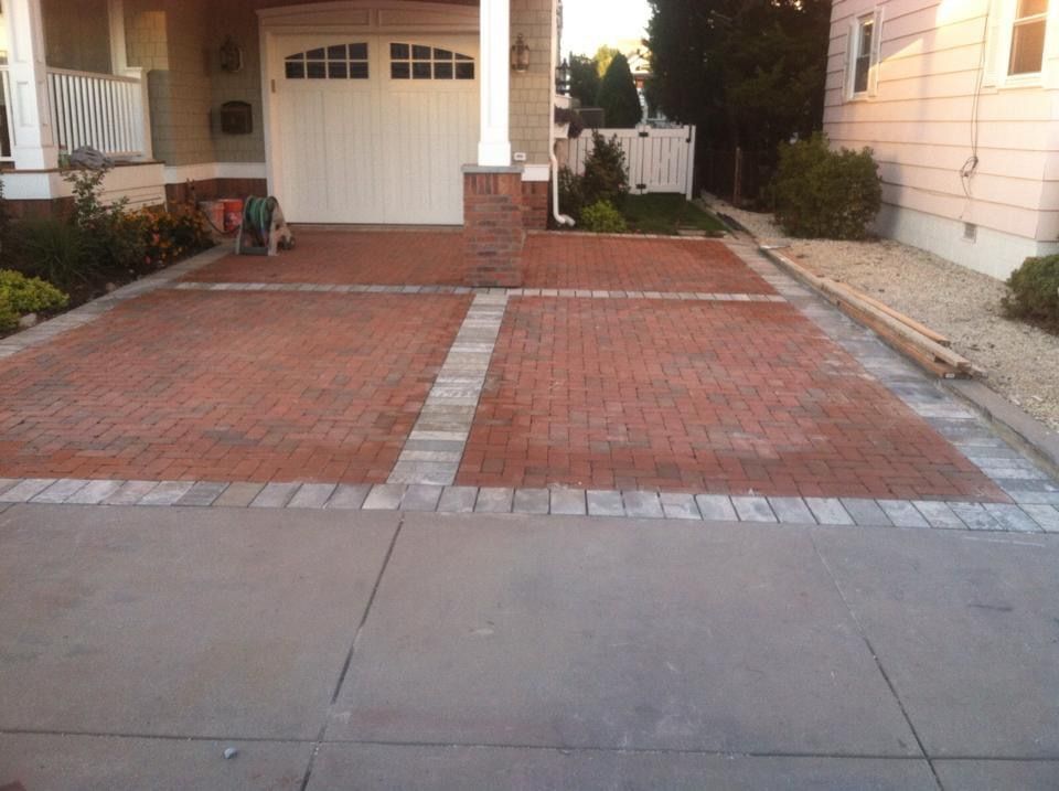 Brick driveway with concrete apron, bordered by gray pavers, leading to a garage.