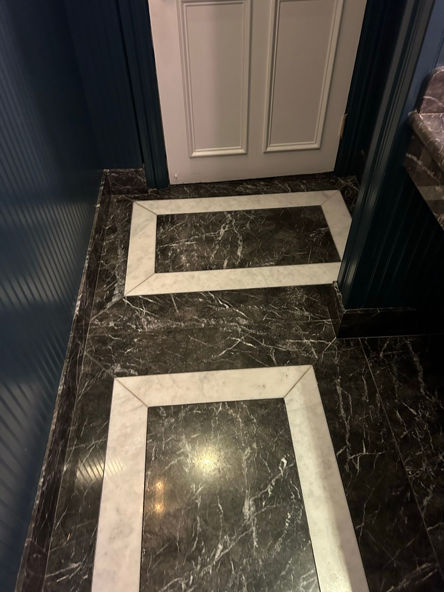 Black marble floor with white-bordered rectangular inlays leading to a white door.