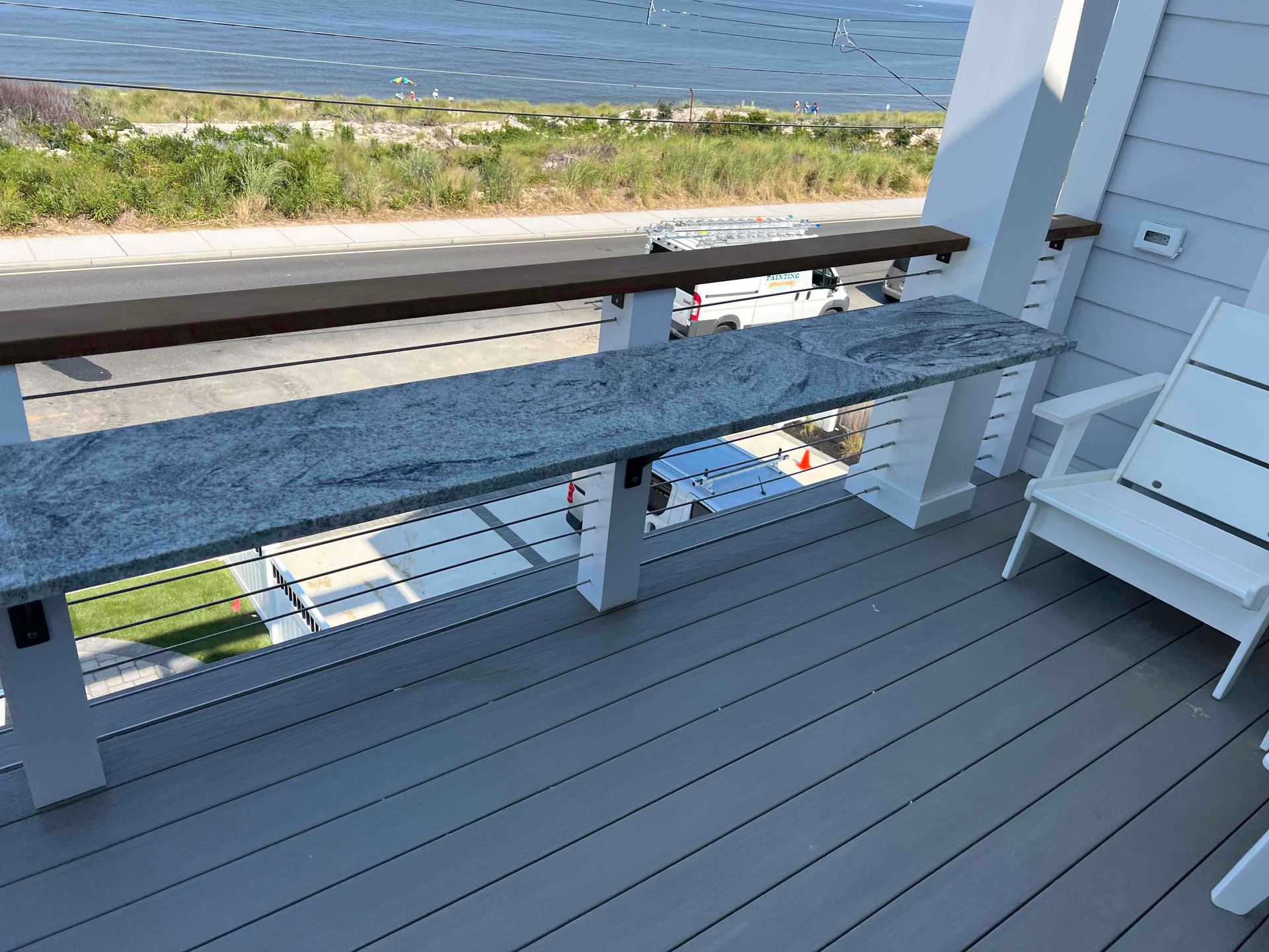 A gray granite outdoor bar with a water view. A white chair sits nearby on a gray deck.