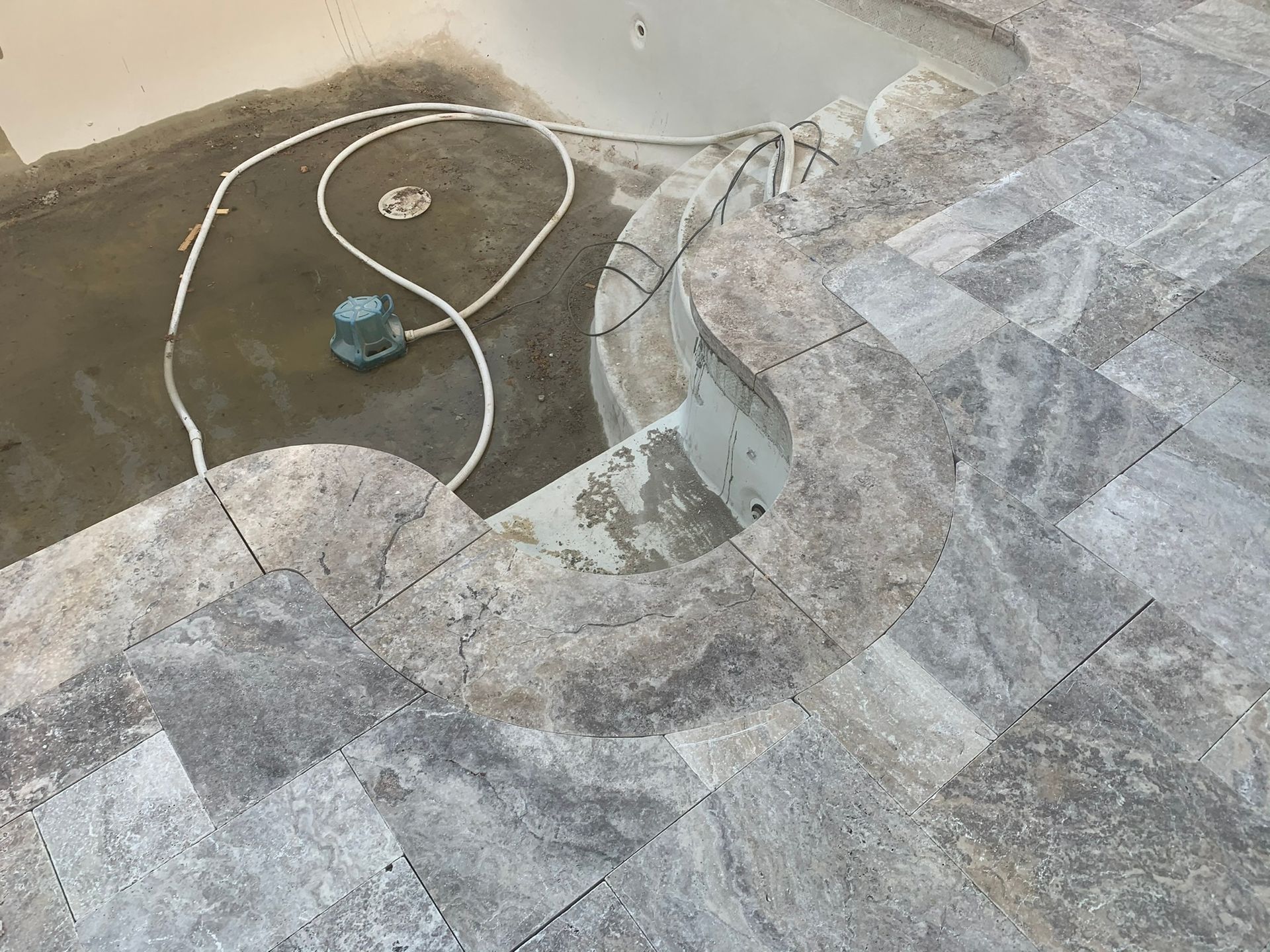 Poolside, partial view. Water pump and hose by a curved pool edge with gray tile.