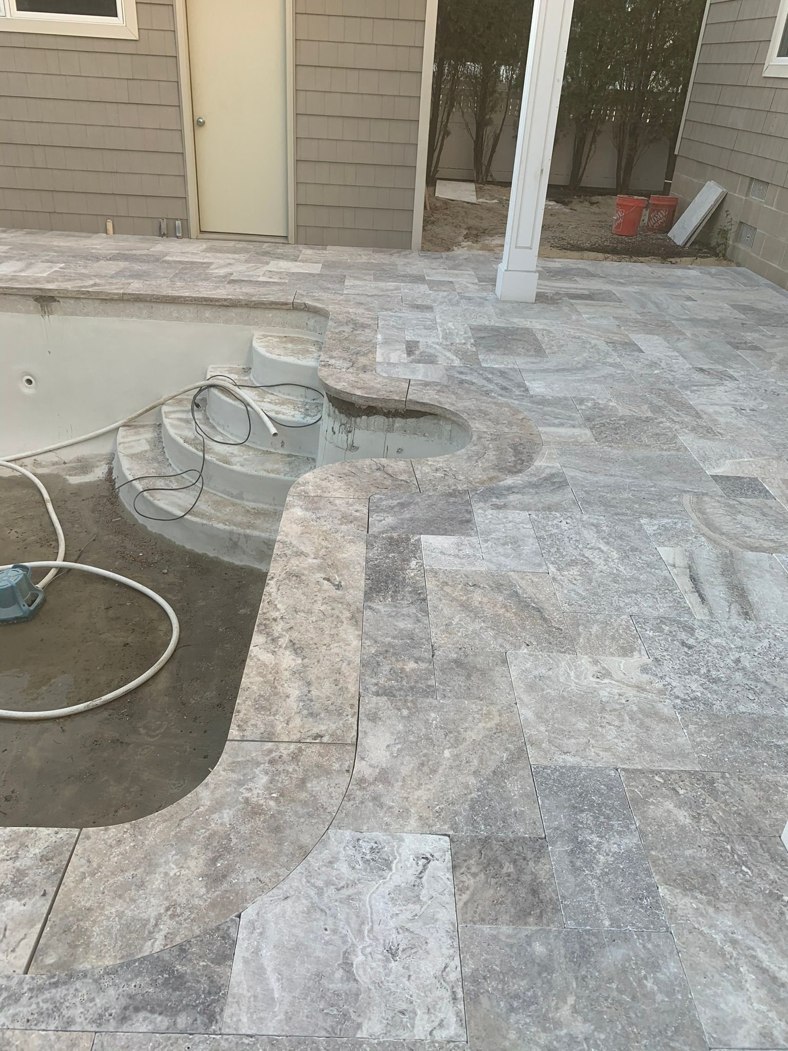 Patio with gray stone, pool stairs, white pillar, and partially finished pool.
