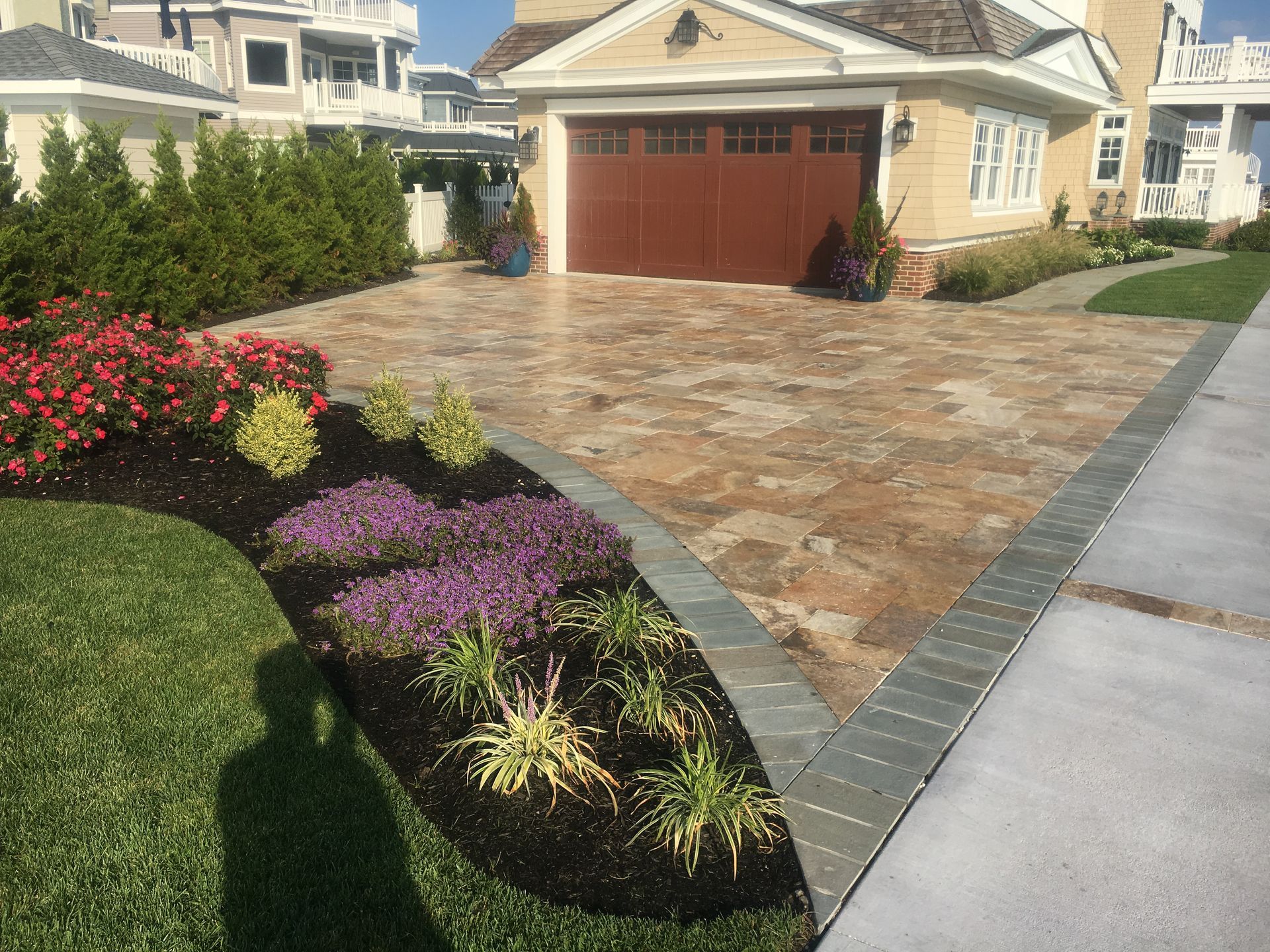Stone driveway with colorful flower beds and a brown garage door.