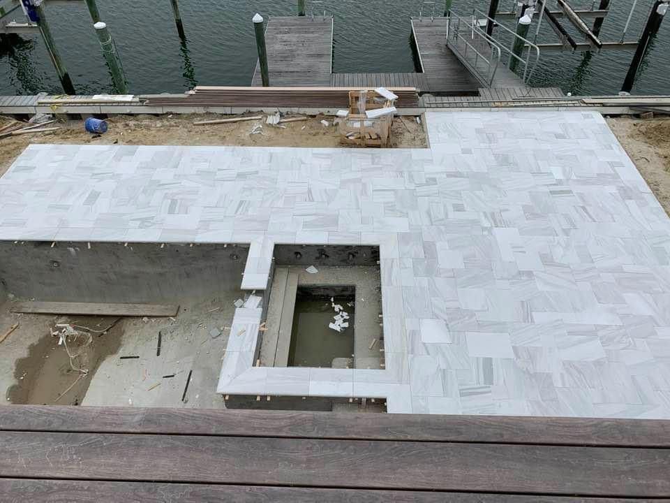 Construction site near water: gray tiled patio around a pool area.