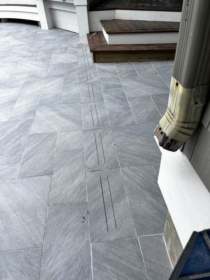 Gray stone pavers lead to a set of stairs, with a downspout and drainage slits in the pavement.