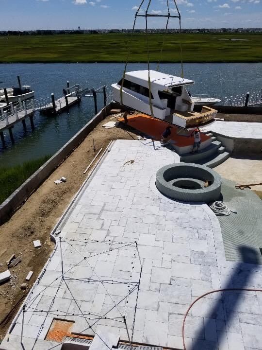 A boat being lifted by a crane near a dock and a newly paved patio.