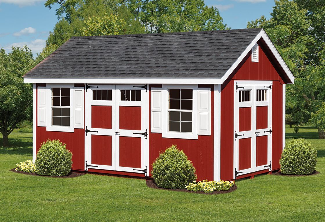 a red shed with white shutters is sitting in the middle of a lush green field .