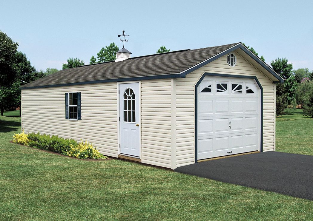 a white garage with a black roof is sitting on top of a lush green field .
