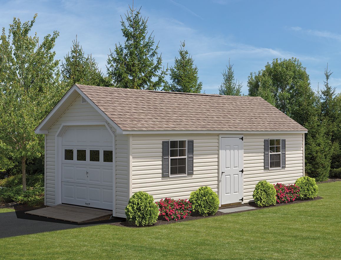 a white garage with a brown roof is sitting on top of a lush green lawn .