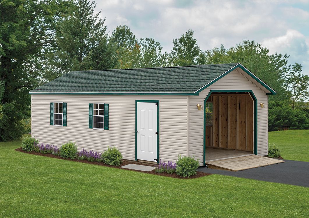 a white garage with a green roof is sitting in the middle of a lush green field .