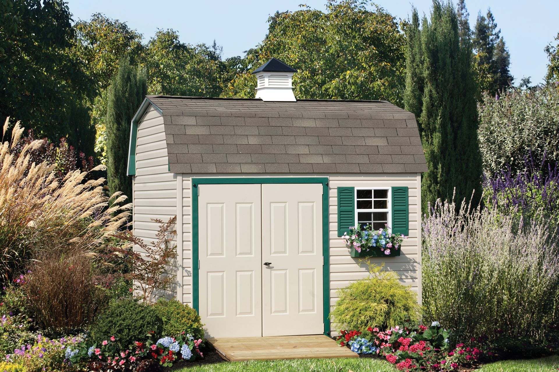 a white shed with green shutters sits in the middle of a garden