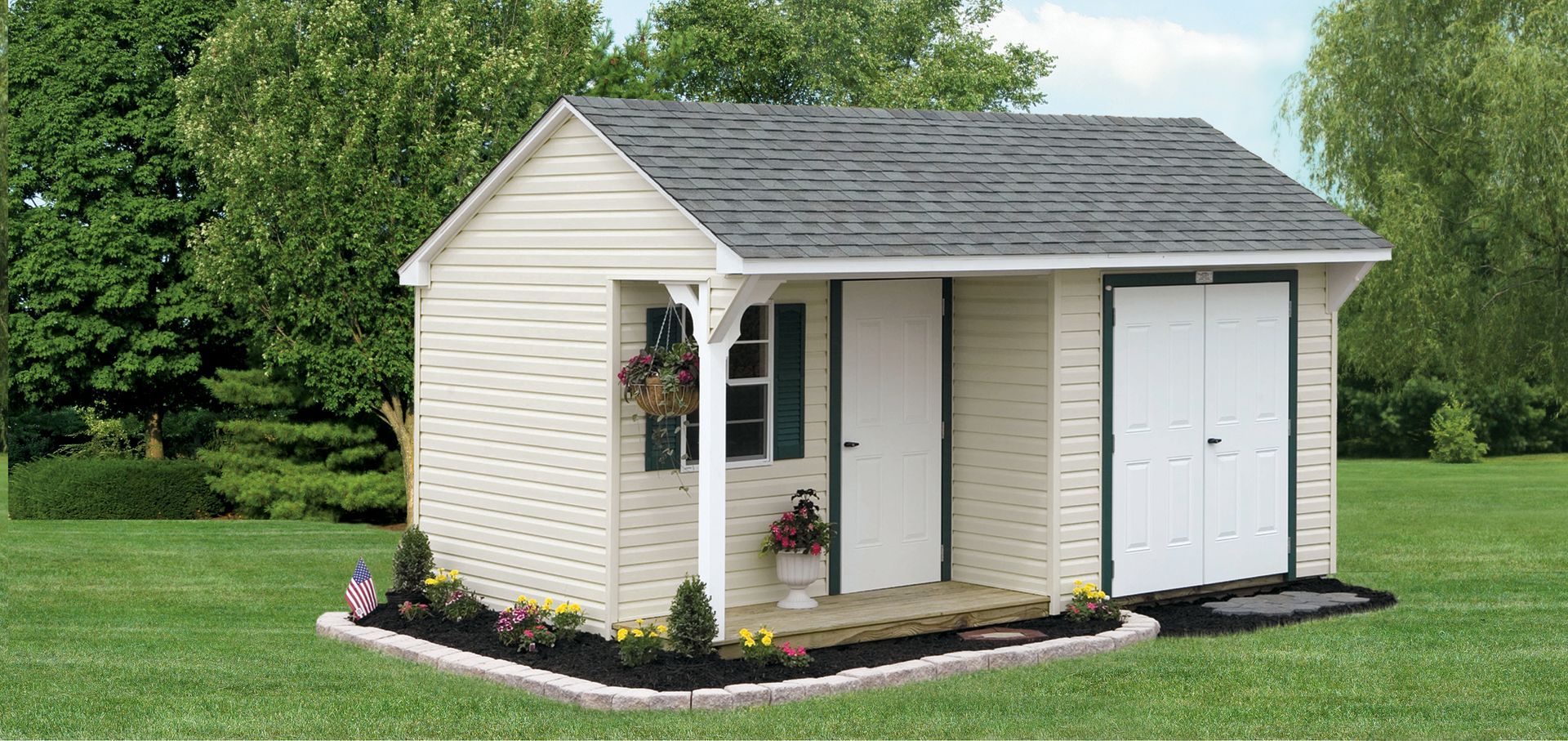a white shed with a gray roof is sitting in the middle of a lush green field .