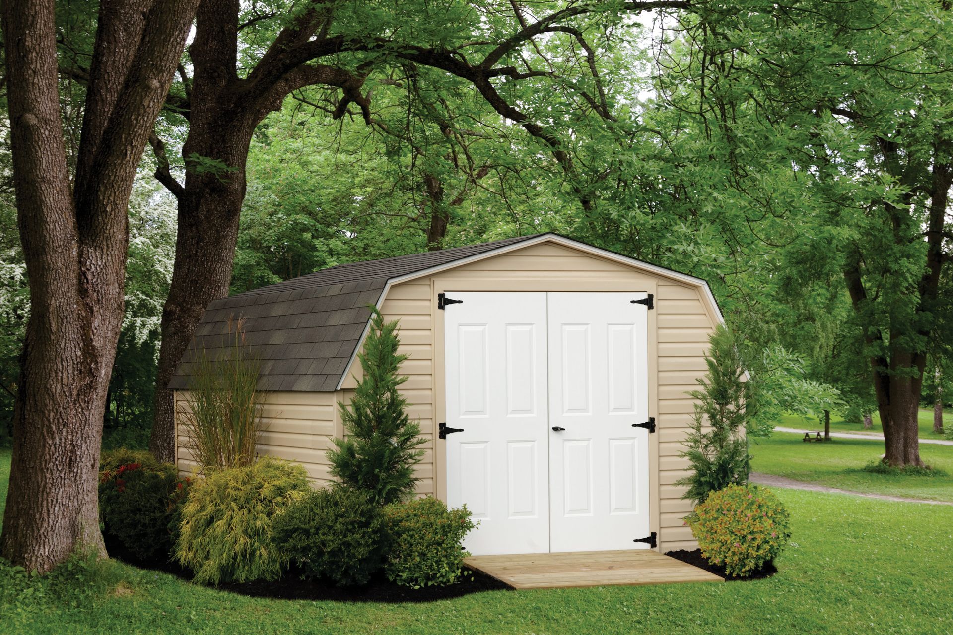a tan shed with white doors is surrounded by trees in a yard .