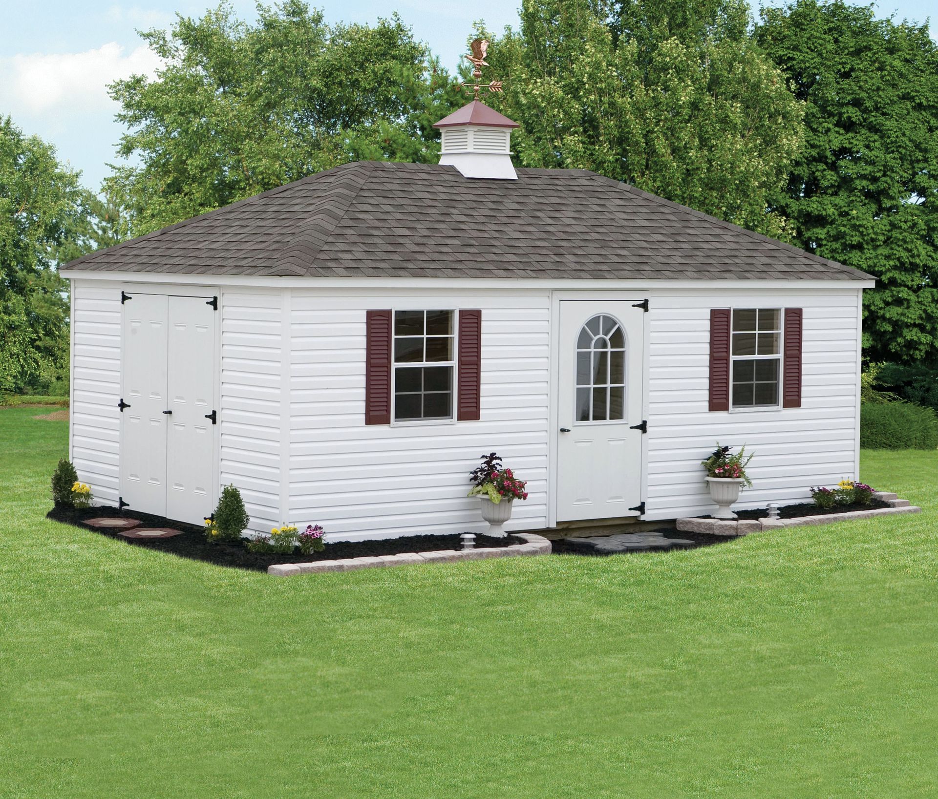 a white shed with brown shutters sits in the middle of a lush green field