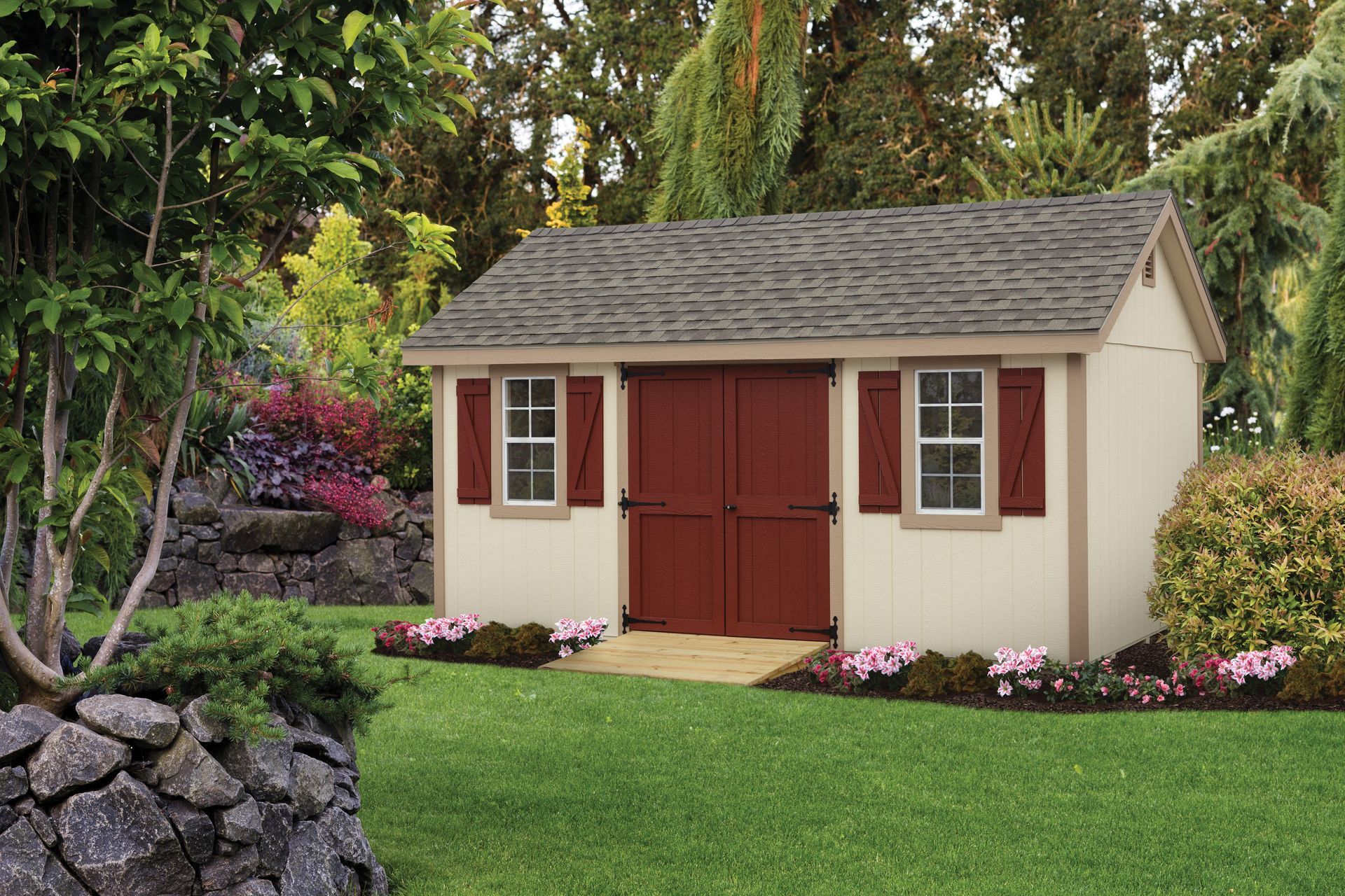 a white shed with red doors and shutters is in the middle of a lush green yard .