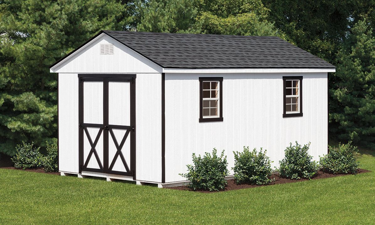 a white shed with black trim is sitting in the middle of a lush green field .