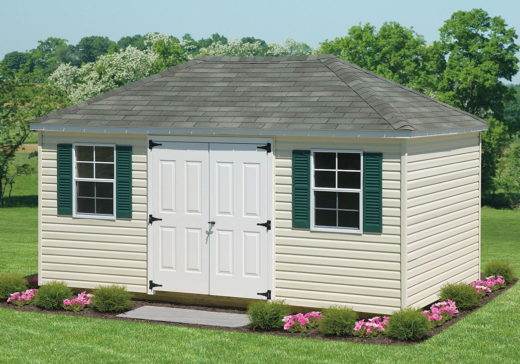 a white shed with green shutters is sitting in the middle of a lush green field .