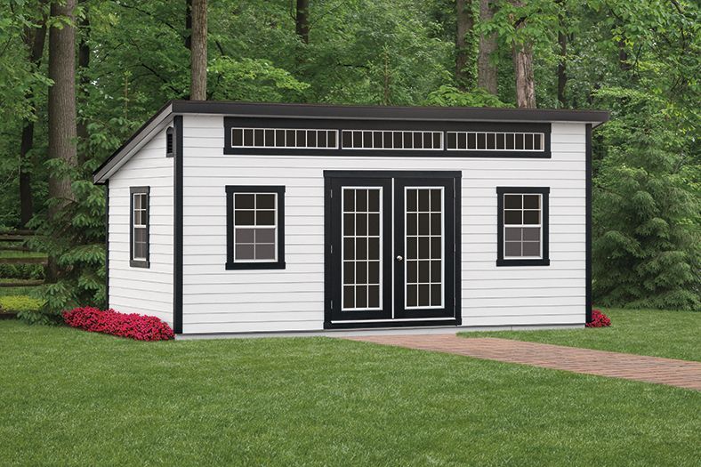 a white shed with black windows and doors is sitting on top of a lush green lawn .
