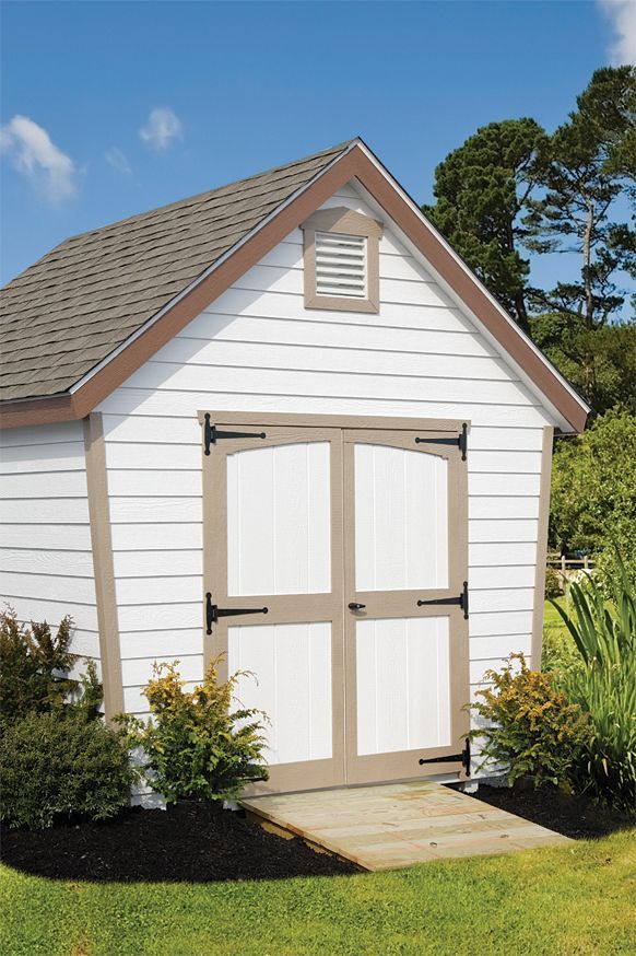 a white shed with brown trim sits in the grass