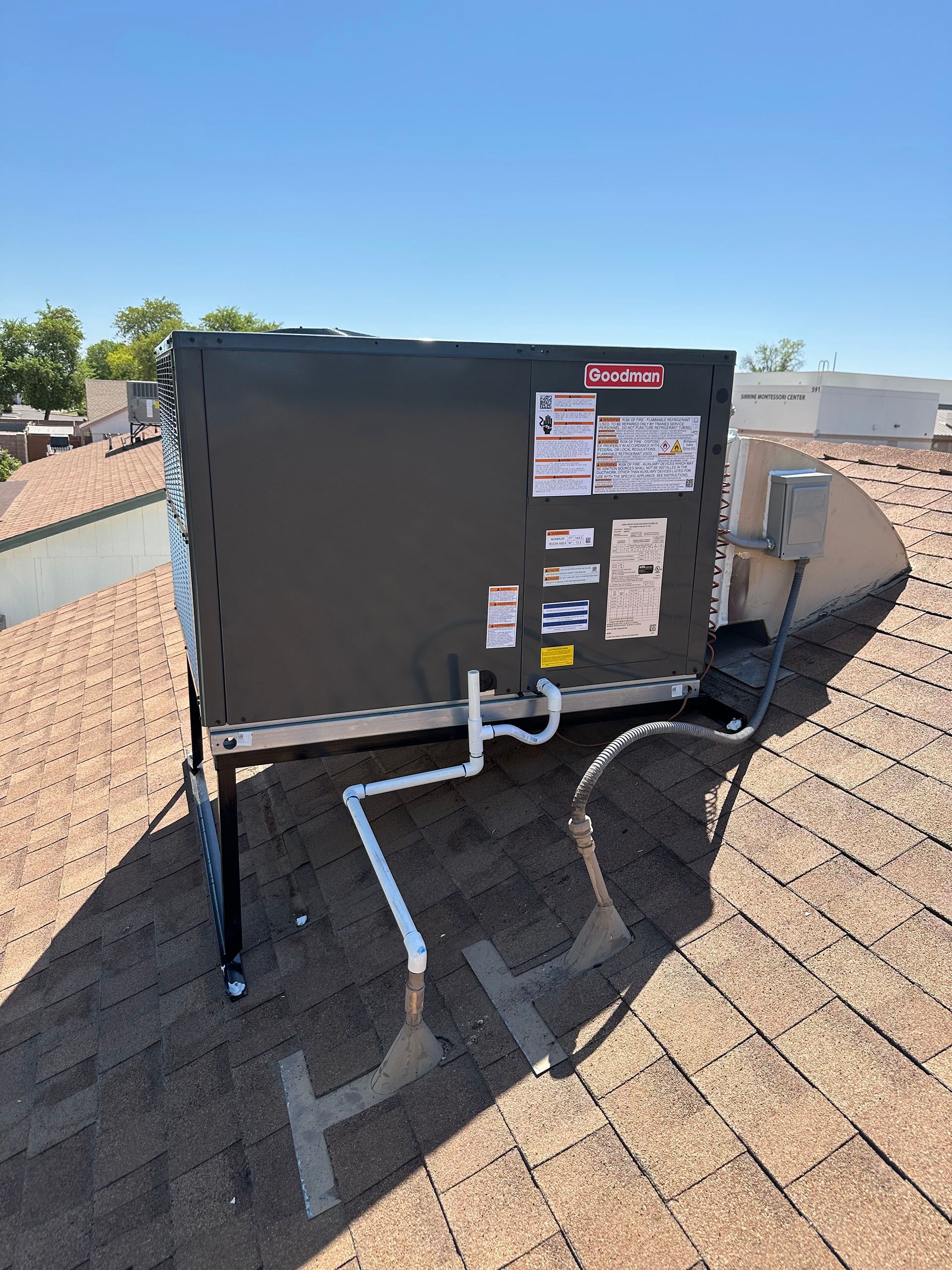 Outdoor HVAC unit on a rooftop with metal piping and a clear blue sky in the background.