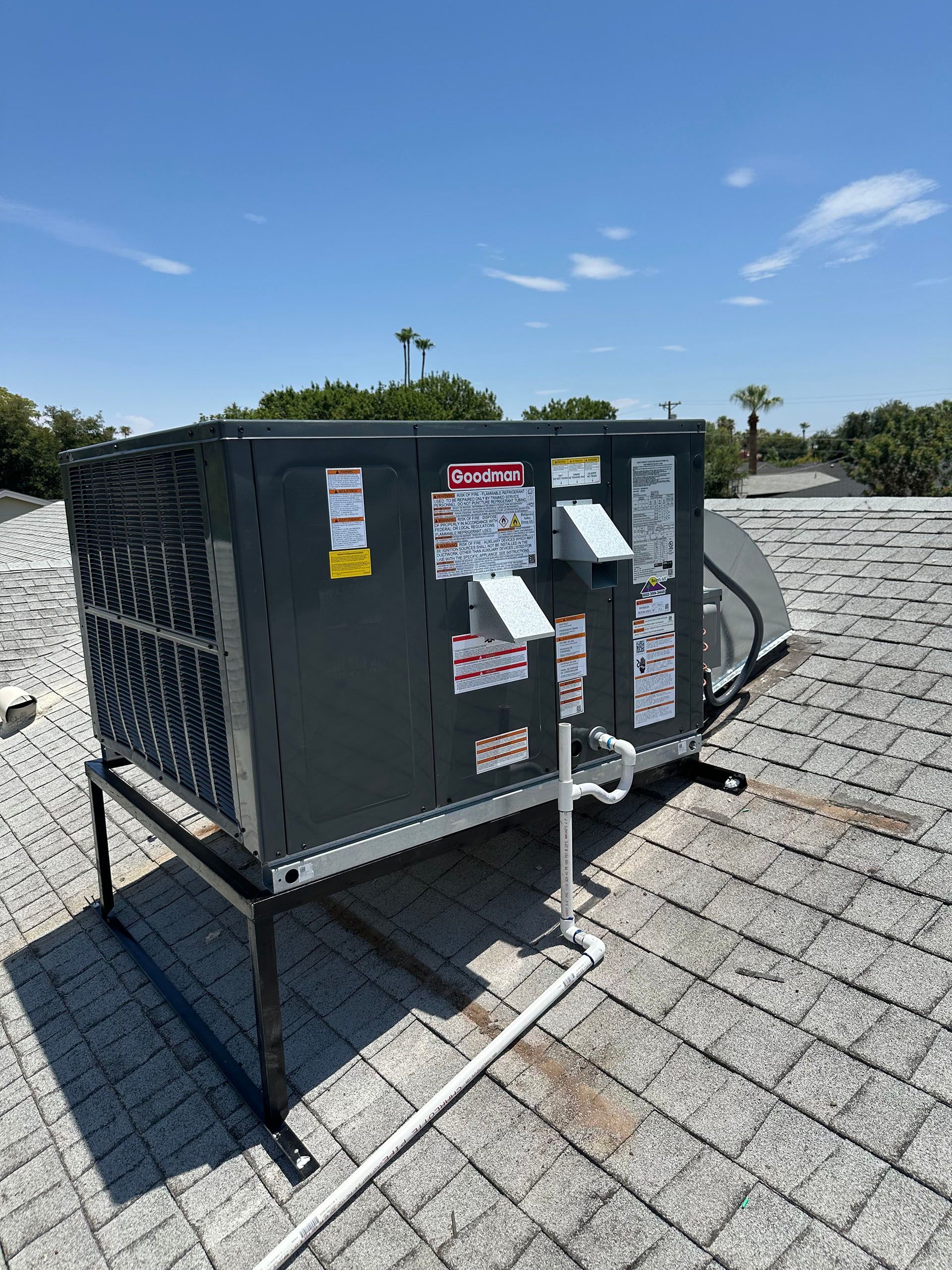Large gray rooftop HVAC unit with warning stickers on a gravel rooftop under a clear blue sky.