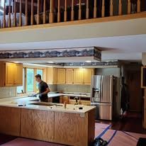 Man in kitchen near construction, cabinetry and upper level.