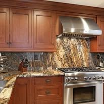 Kitchen with brown cabinets, stainless steel range hood, and marble backsplash.