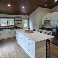 A bright kitchen with a white island and dark wood ceiling.
