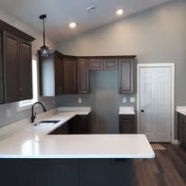 Kitchen with white countertops, dark cabinets, a window, and a white door.