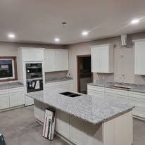 Kitchen with white cabinets, island with granite countertop, built-in oven, and stainless steel appliances.