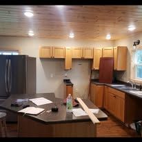 Kitchen with wooden ceiling, cabinets, and island. Stainless steel refrigerator on the left.