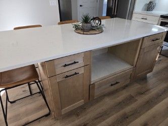 Kitchen island with a light countertop, wood cabinets, and bar stools.