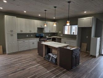 A newly constructed kitchen with light cabinets, dark island, wood floor, and three pendant lights.