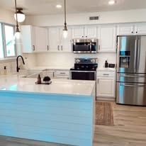 Modern kitchen with white cabinets, island, stainless steel appliances.