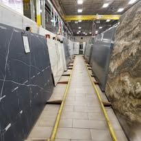 Large slabs of stone in a warehouse. A narrow walkway with yellow borders leads to the stones.