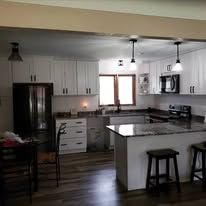 Kitchen with cabinets, island, and dining area. Neutral colors with pendant lights.