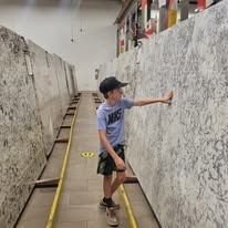 Boy in a Nike shirt and cap examines large slabs of stone in a warehouse.