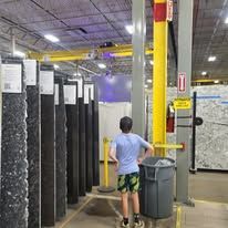 Person standing in front of granite slabs in a store, looking up. A crane system is above.