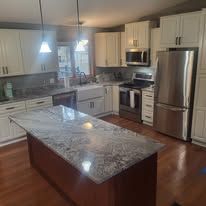 Kitchen with large island, stainless steel appliances, white cabinets, and granite countertops.