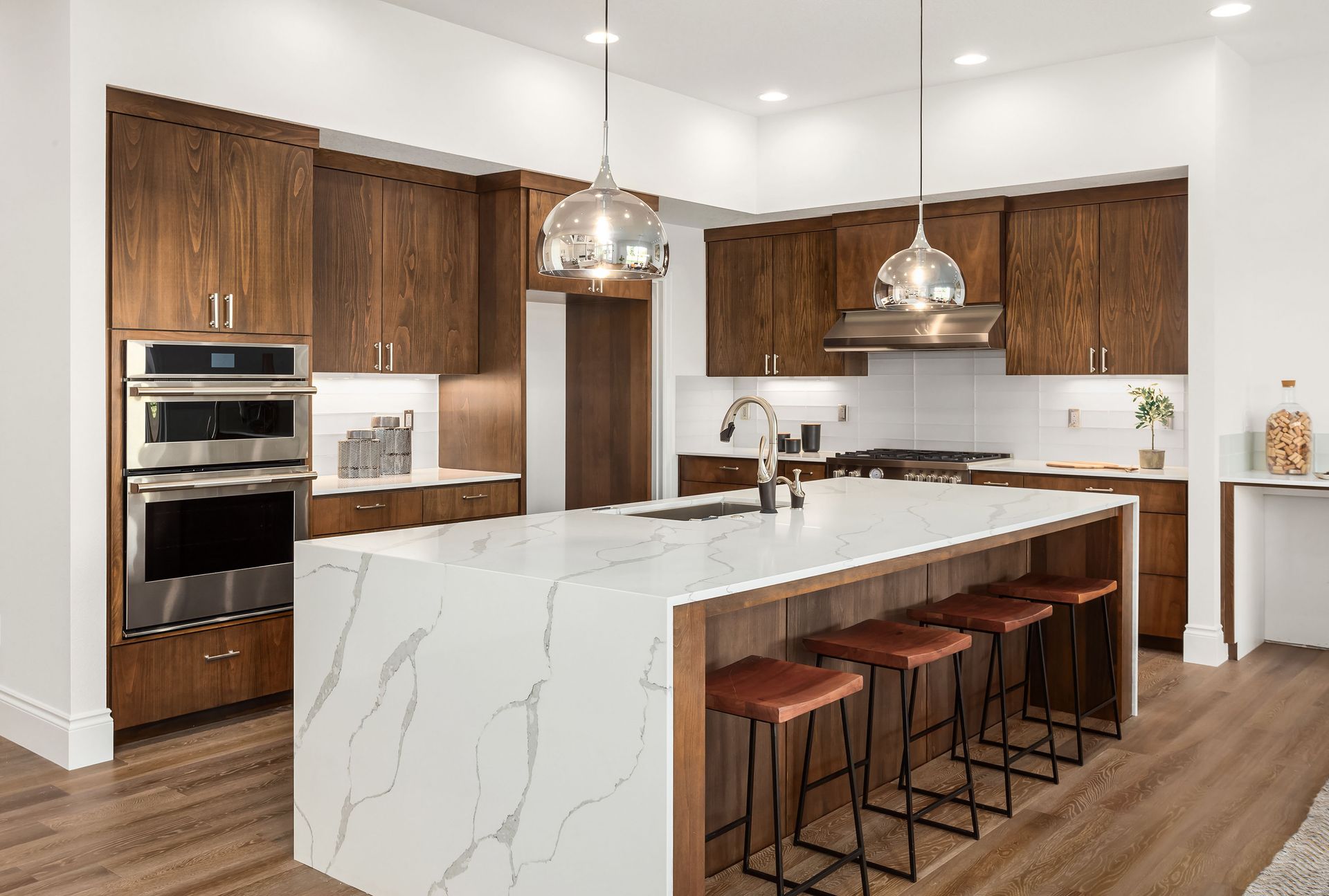 Modern kitchen with wood cabinets, white countertops, island with bar stools, and stainless steel appliances.