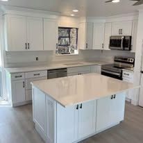 A well-lit modern kitchen with white cabinets, countertops, and stainless steel appliances.