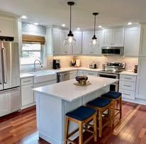 Modern kitchen with white countertops, island, and seating. Light fixtures hang above.