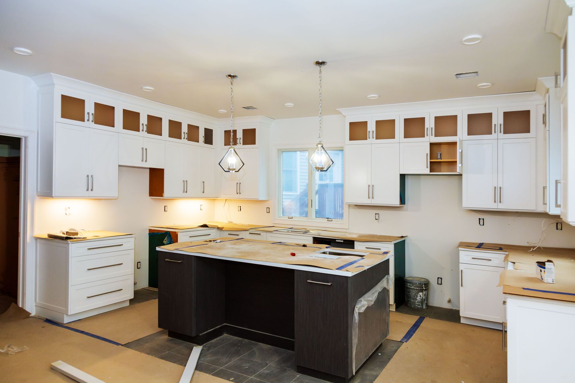 Kitchen under construction with white and dark cabinets, a center island, and exposed walls.