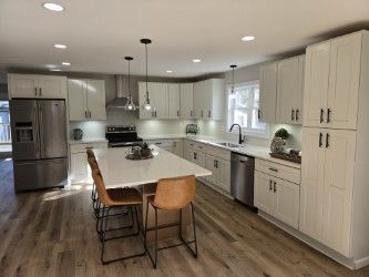 Spacious white kitchen with island, stainless steel appliances, light wood floors, and bar seating.