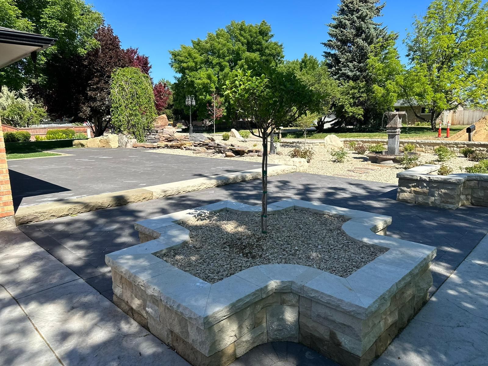 Stone planter with a young tree in a sunny landscaped courtyard with gravel and paving stones