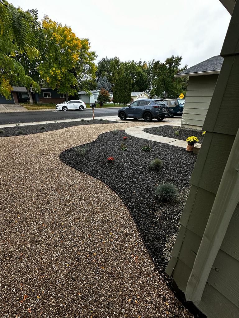 Front yard with dark mulch, shrubs, and a driveway; parked cars and leafy trees across the street.