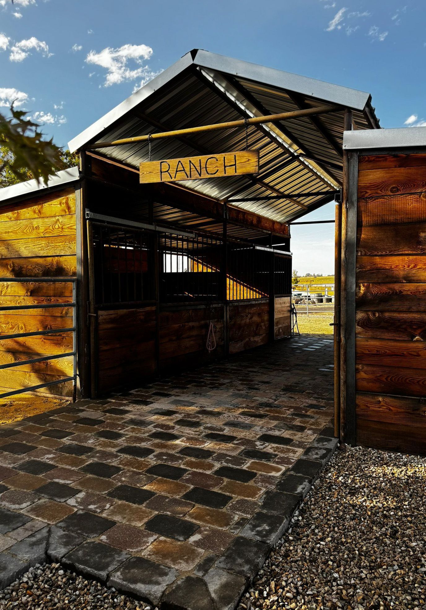 Open wooden gate leading to a rustic entrance with a tiled path under a bright sky