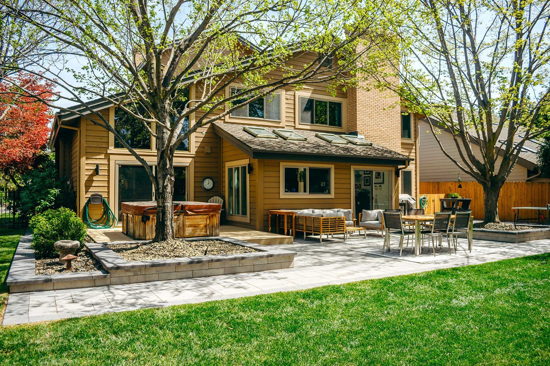 Backyard patio with outdoor dining set beside a two-story house and green lawn